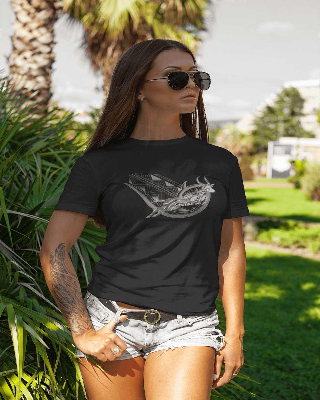 RUGBYNOMAD black organic cotton womens classic streetwear t shirt with tribal south africa artistic design,f emale model standing hand in pocket, wearing jean shorts, black sunglasses, green trees background Edit